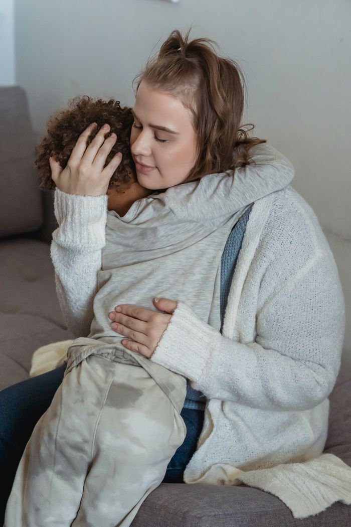 Blog Affectionate mother sitting in comfortable sofa and embracing crying child with dark curly hair at home